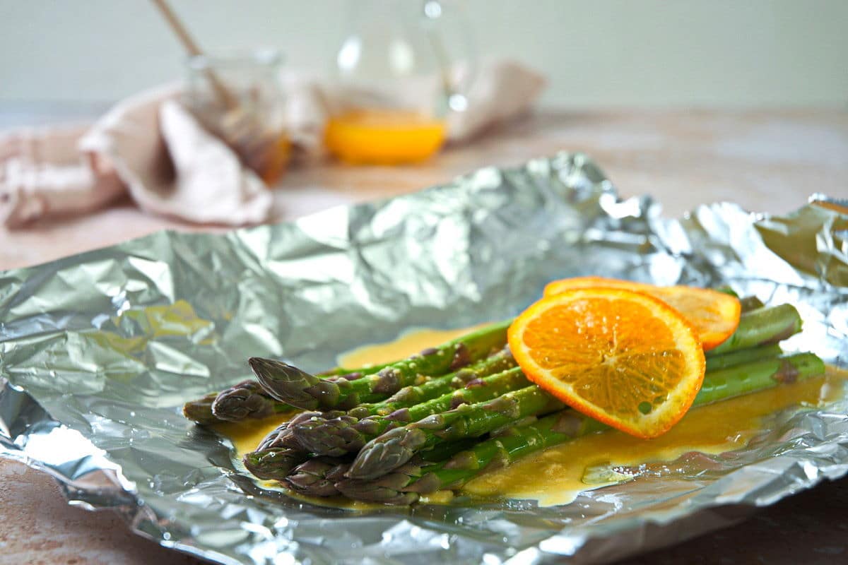 Raw asparagus with orange slices on foil.