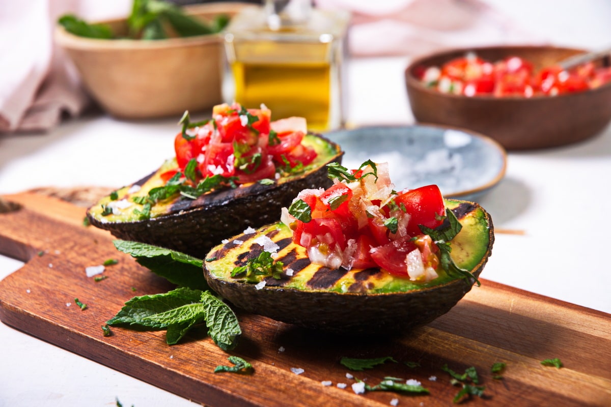 Close up of grilled, stuffed avocados on wooden cutting board.