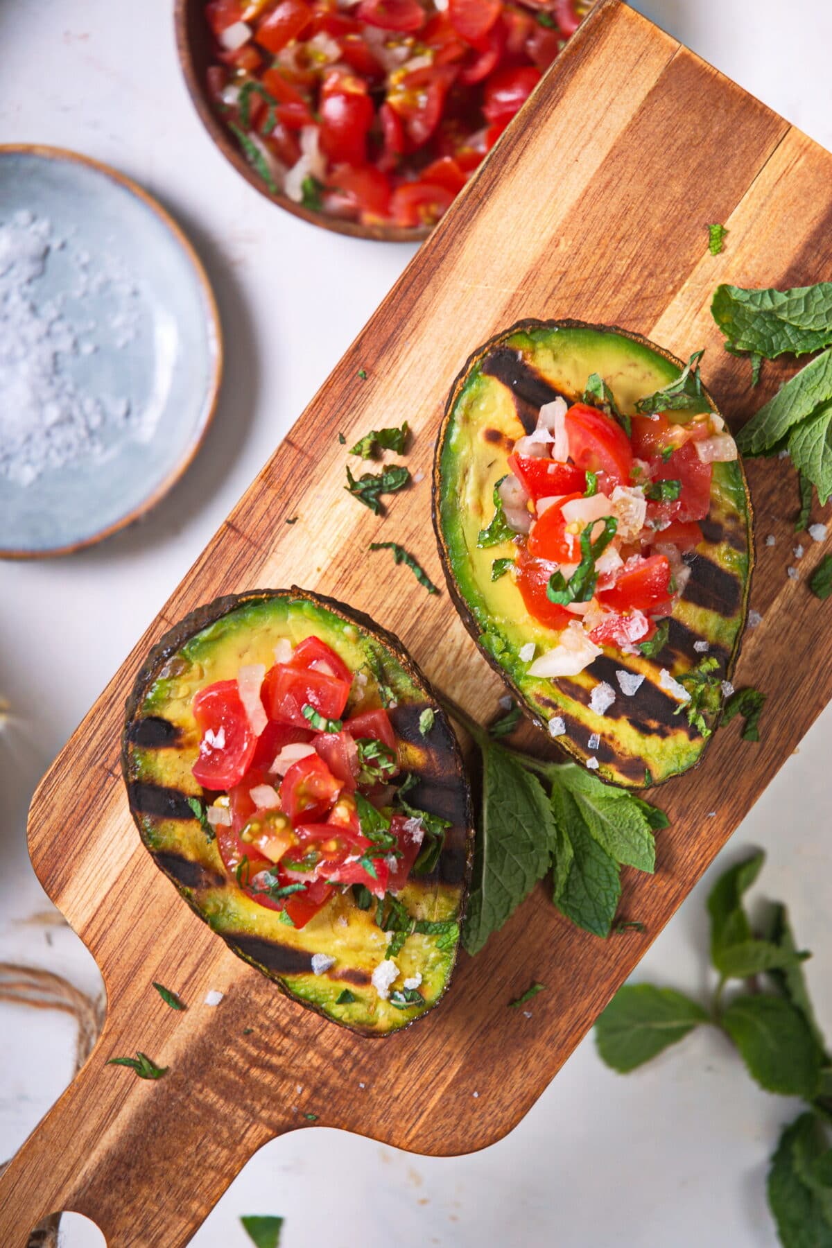 Top view of stuffed, grilled avocadoes on wooden cutting board.