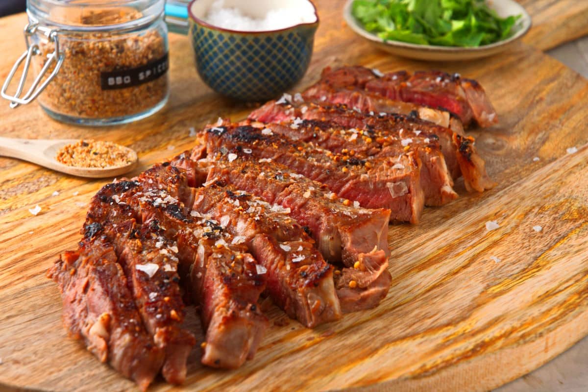 Grilled bison ribeye steak sliced on wooden serving board.