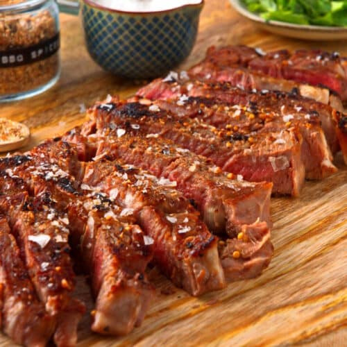 Grilled bison ribeye steak sliced on wooden serving board.