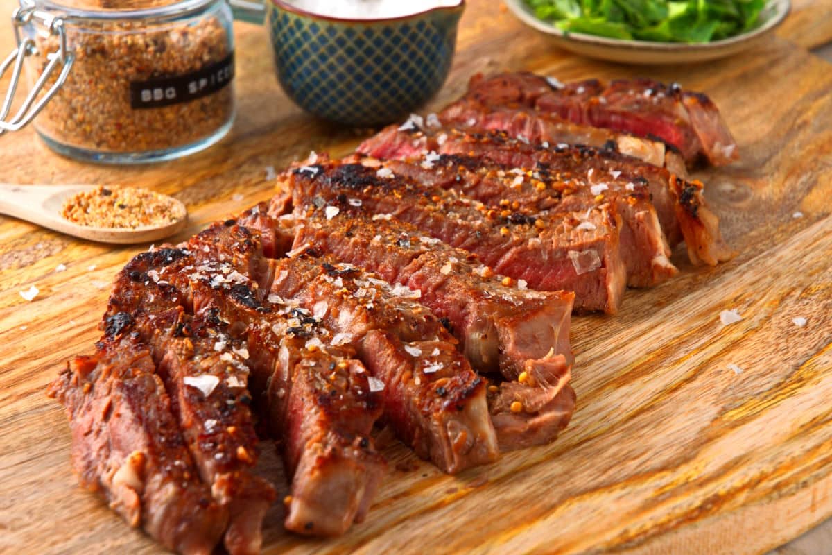 Grilled bison ribeye steak sliced on wooden serving board.