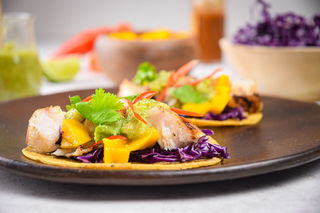 Grilled halibut tacos on brown wooden plate.