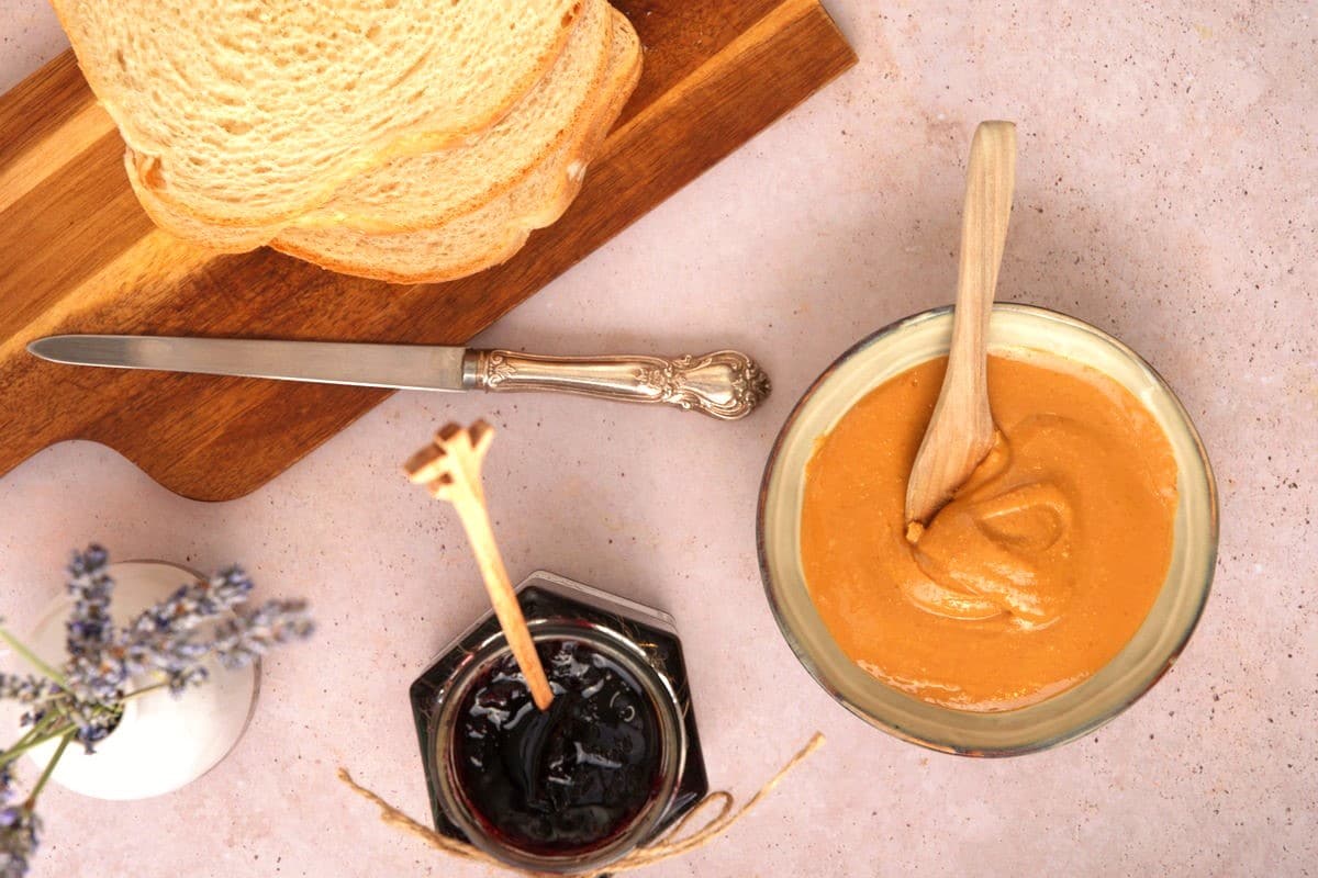 Peanut butter and jelly in jars with bread slices on the side.