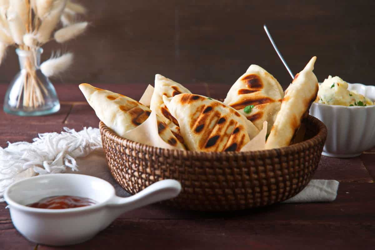 Grilled pierogies in wooden basket with BBQ sauce and filling on the side.