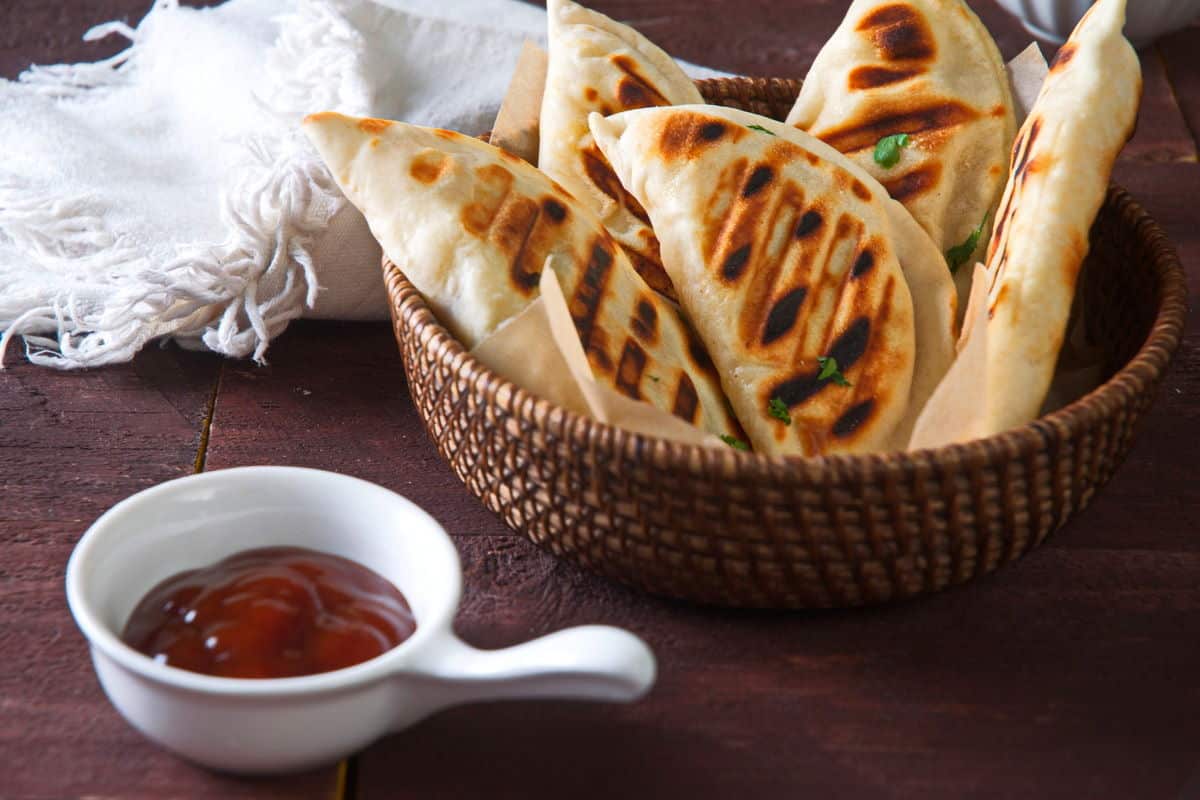 Grilled pierogies in wooden basket with BBQ sauce on the side.