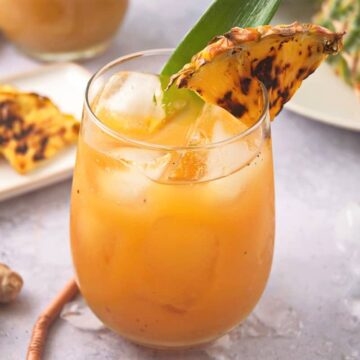 Grilled pineapple juice and wedge in glass with fresh ginger root on the side.