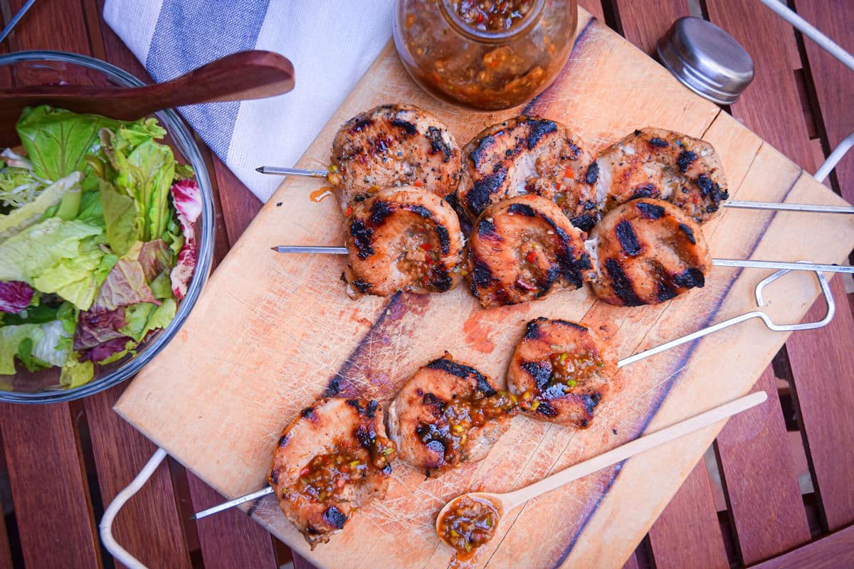 Grilled pork skewers on wooden cutting board with salad and jerk sauce and salad on the side.