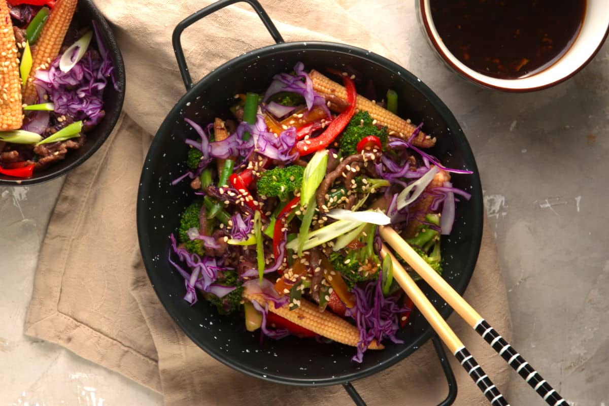 Ground beef and veggie stir fry in black bowl with chopsticks.