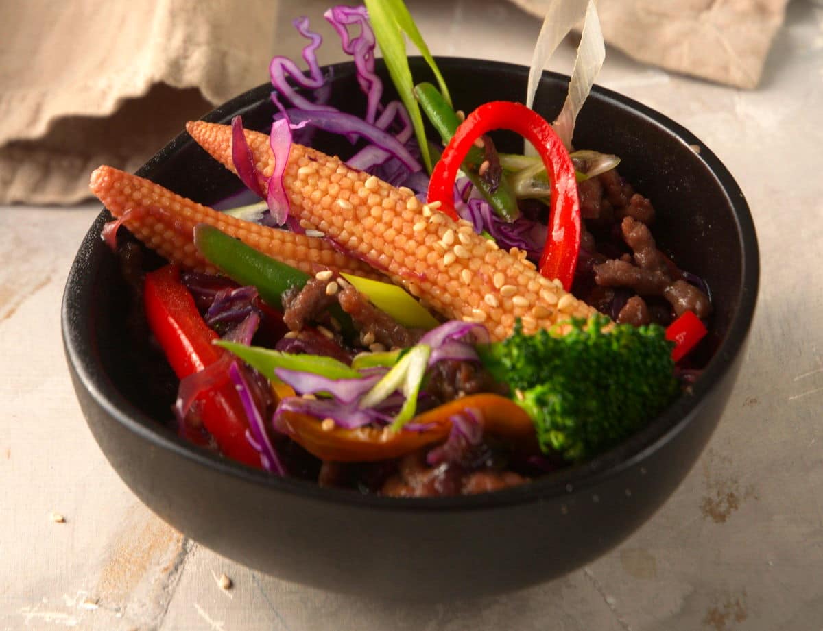 Ground beef and veggie stir fry in black bowl.