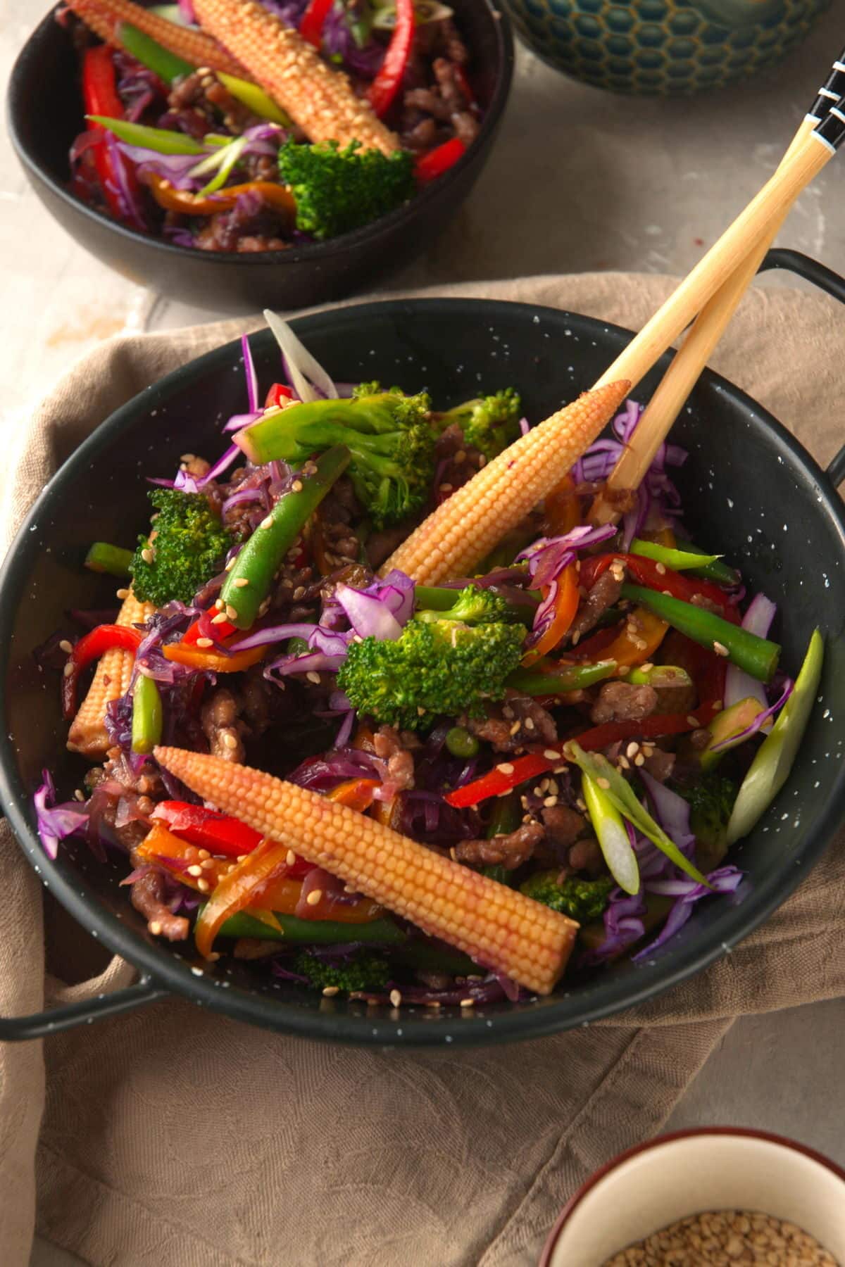 Ground beef stir fry with a range of vegetables in black bowl with chopsticks.