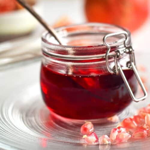 Homemade grenadine in a small glass jar with pomegranate arils around it.