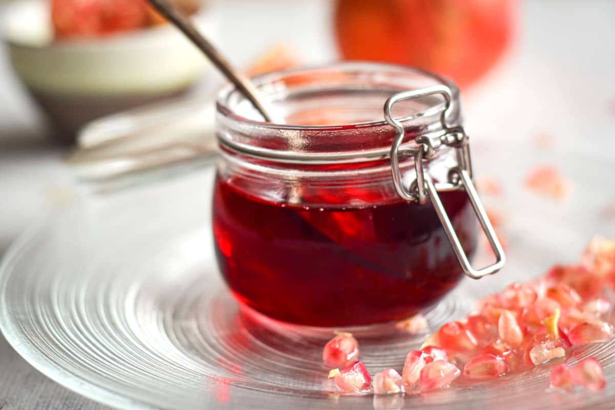 Homemade grenadine in a small glass jar with pomegranate arils around it.