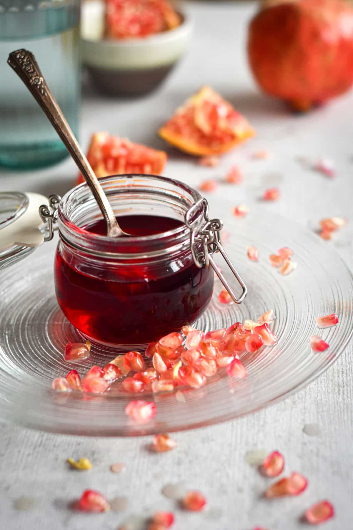 Homemade grenadine in a small glass jar with pomegranate arils around it.