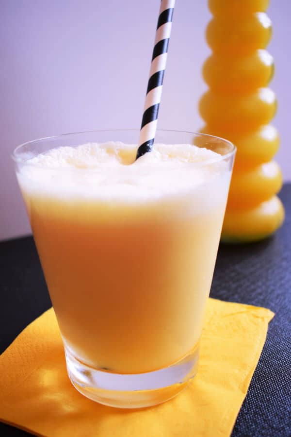 Orange julius in a glass with an orange napkin and bottle of orange juice in the background.