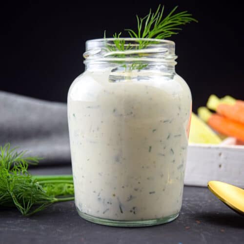Homemade ranch dressing in a jar with fresh dill and a golden spoon on the side.