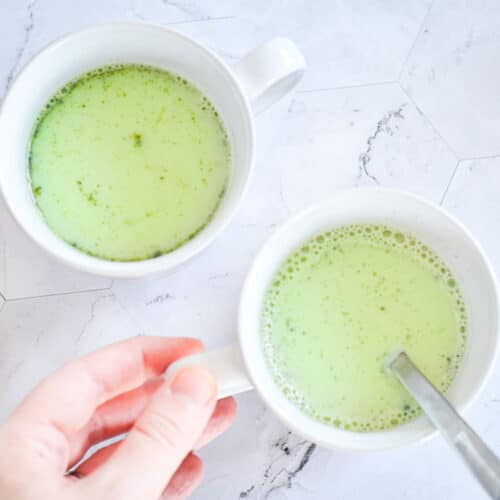 Vegan matcha latte in 2 white mugs with a spoon.