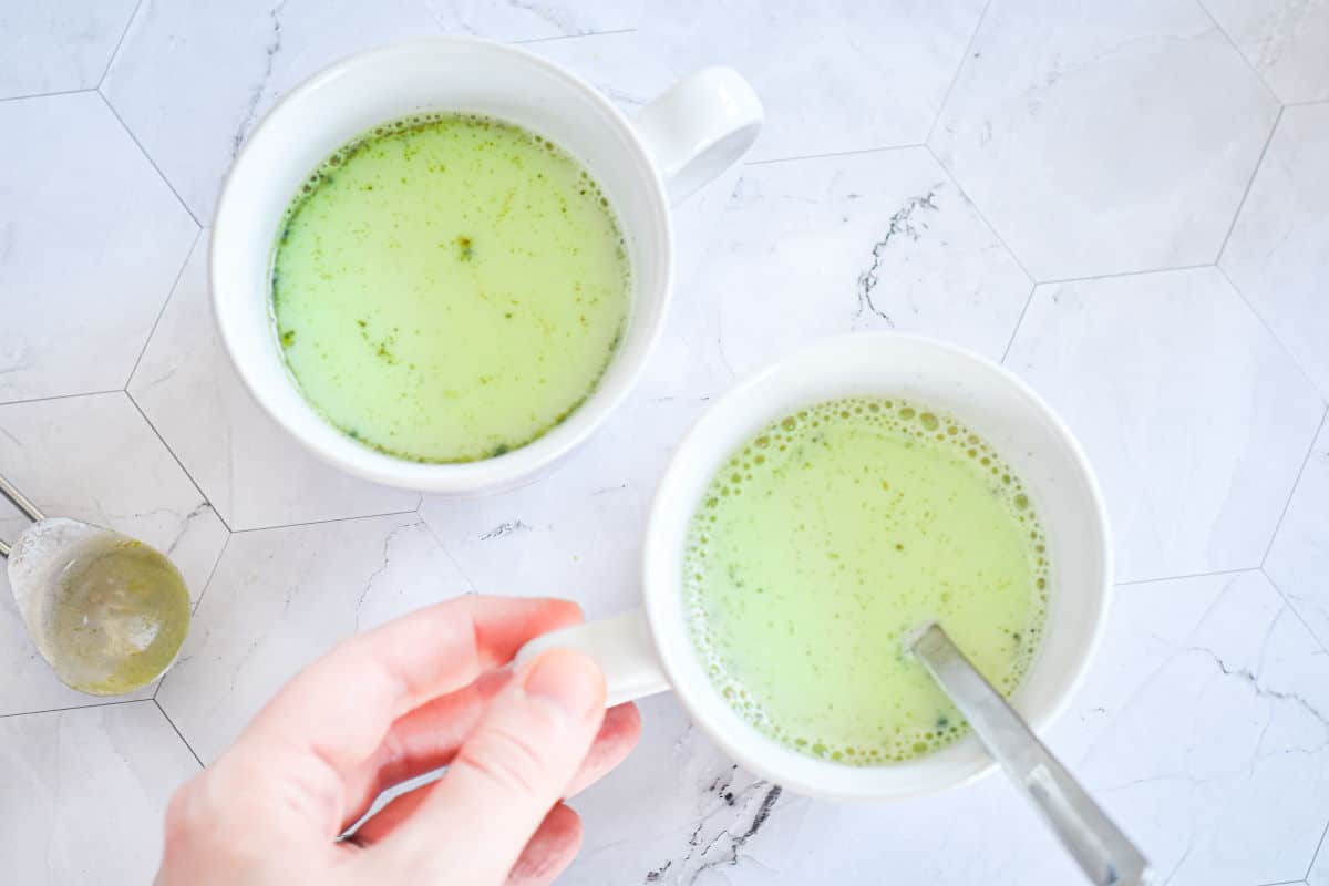 Vegan matcha latte in 2 white mugs with a spoon.