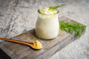 Whipped topping with lemon zest and dill in a small glass jar on wooden background, with a small spoon of mustard powder.