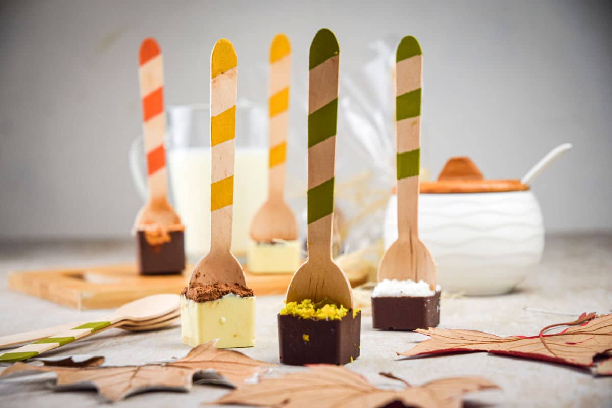 Hot chocolate spoons standing up on light background, surrounded by leaves.