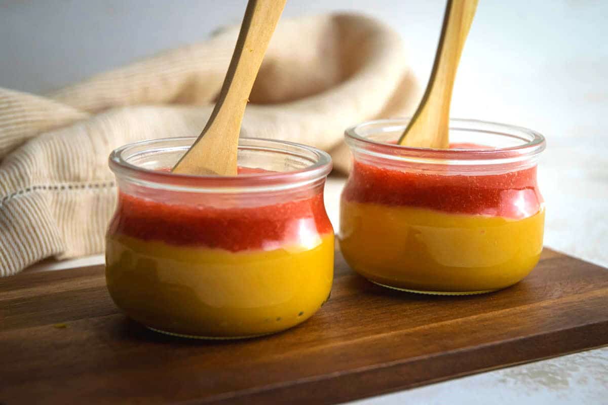 Strawberry puree/coulis in 2 jars of vanilla pudding, on a wooden serving board.