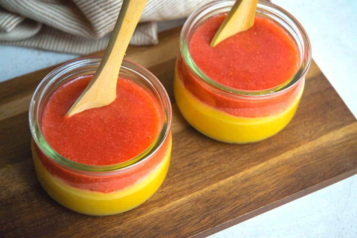 Strawberry puree/coulis in 2 jars of vanilla pudding, on a wooden serving board.