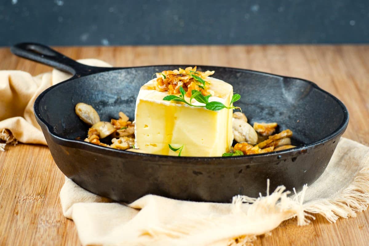 Raw brie wedge in cast iron pan with mushrooms and walnuts.