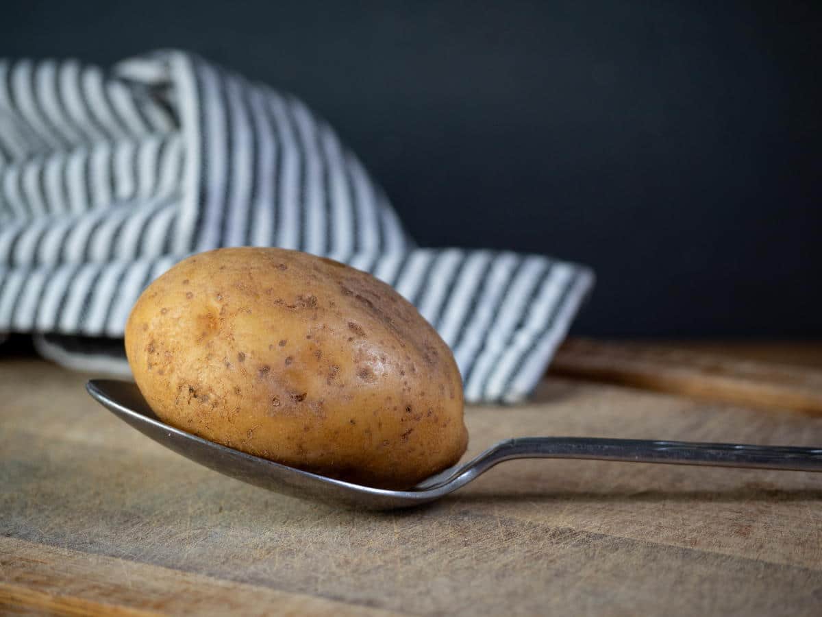 A potato on a spoon, on a cutting board.