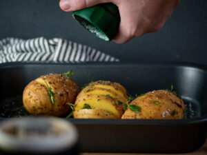 Hasselback potatoes with seasonings in baking dish.