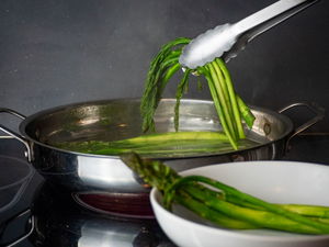 Cooked asparagus in a pan with tongs.