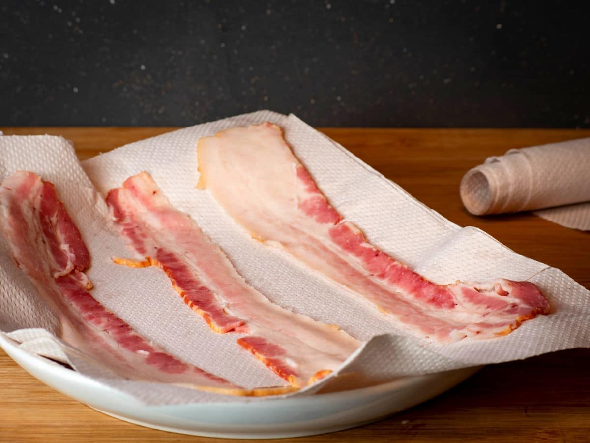 Raw bacon on paper towel-covered plate.