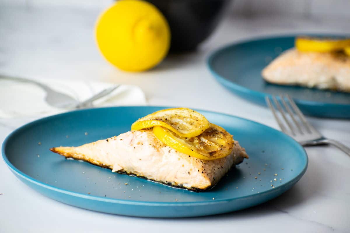 Cooked salmon fillet with lemon slices on blue plate.