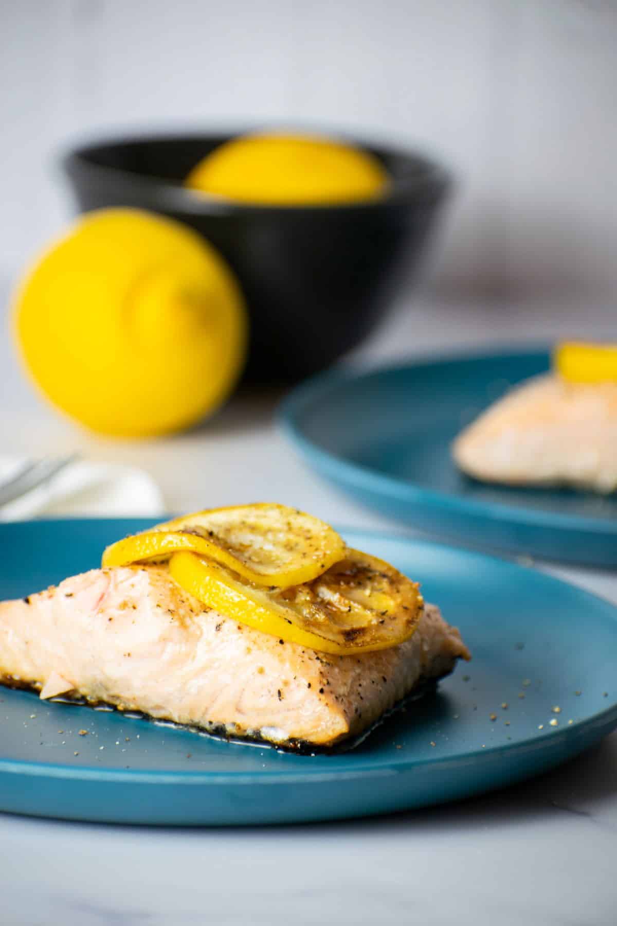 Cooked salmon fillet with lemon slices on blue plate.
