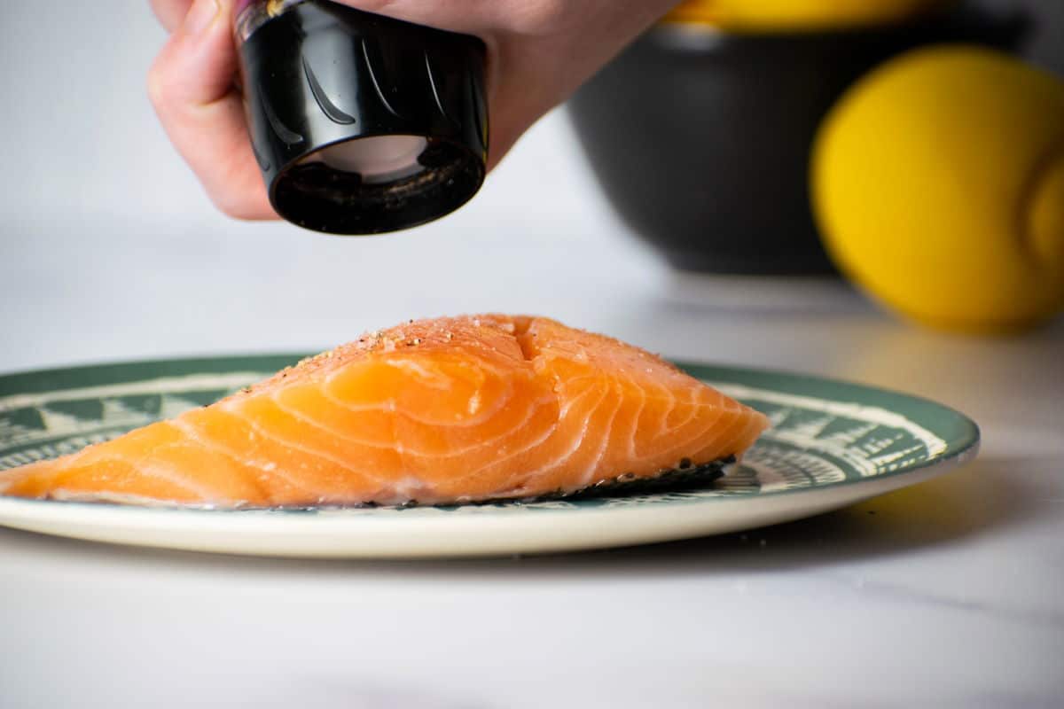 Sprinkling pepper onto salmon fillets.