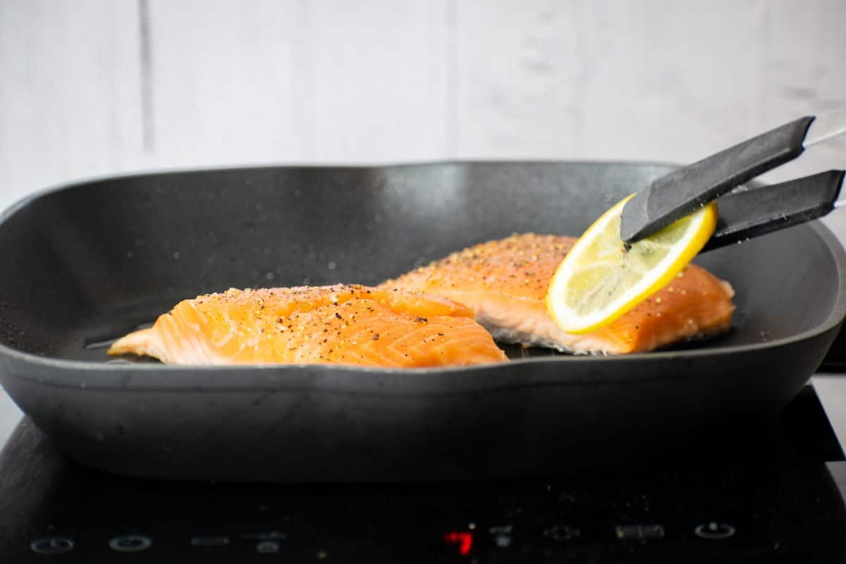 2 salmon fillets in pan with a lemon slice.