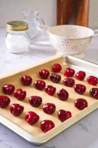 Pitted cherries on pan on marble countertop.