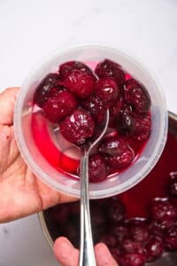 Cherries in a sugar syrup in plastic container with spoon.