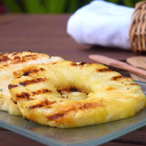 Grilled pineapple slices on glass serving dish on wooden table.