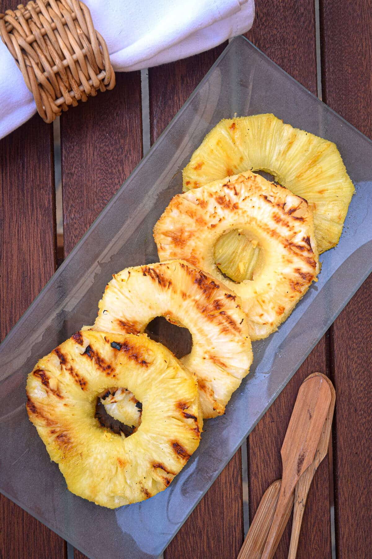 Grilled pineapple slices on glass serving dish on wooden table.