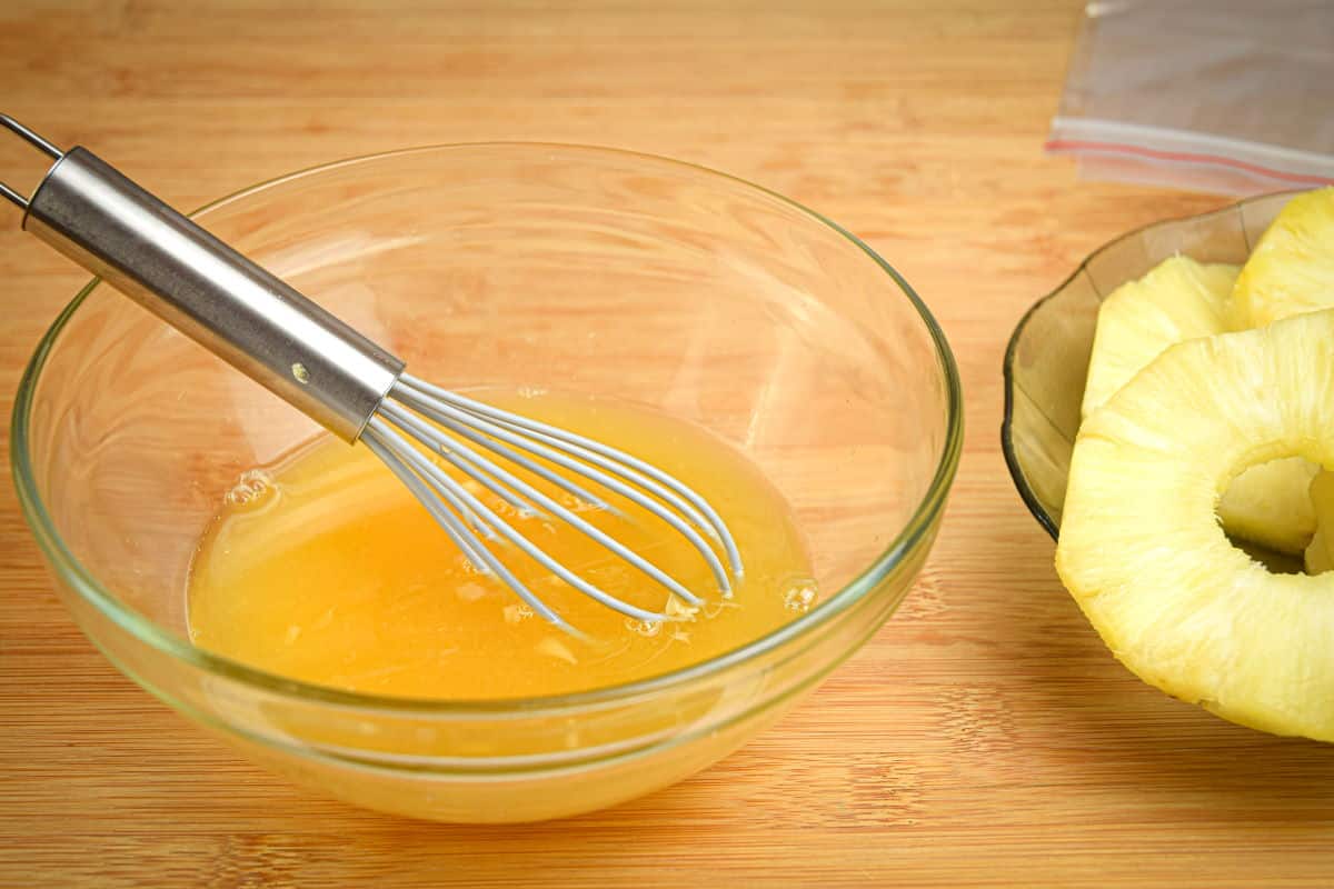 Orange juice marinade in a small glass bowl with pineapple slices on the side.