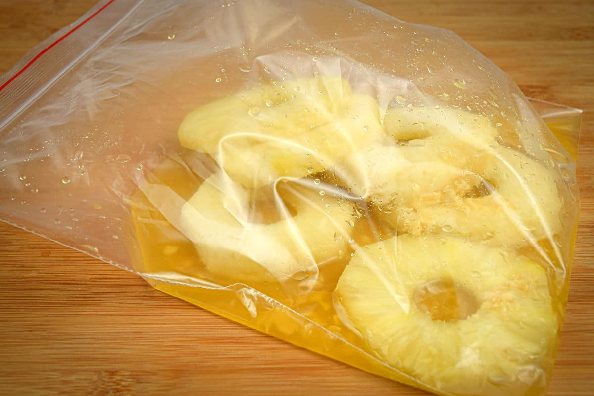 Marinated pineapple slices in a zip top bag.