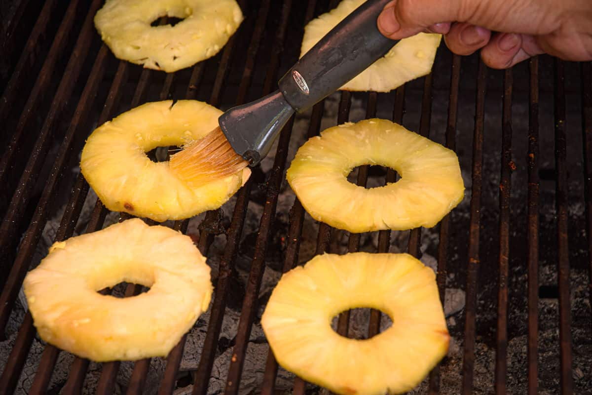 Pineapple slices on outdoor grill with basting brush.