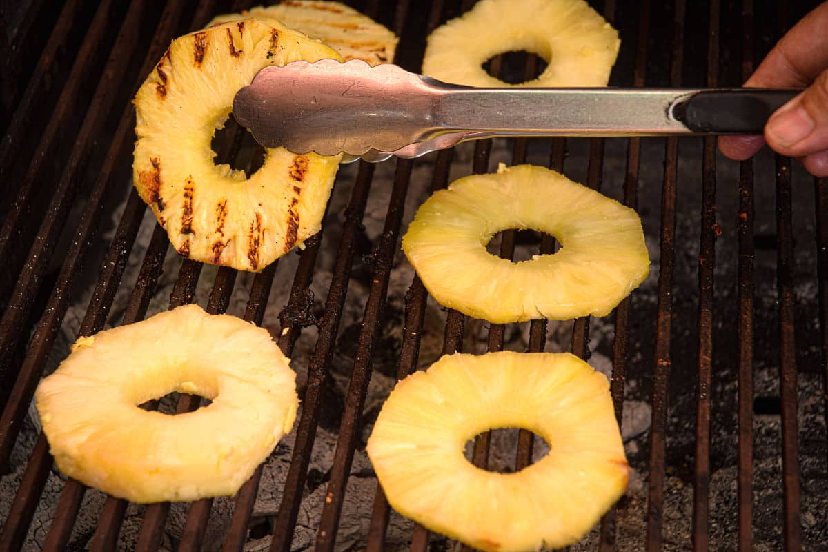 Pineapple slices on the grill with tongs.