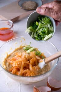 Kimchi pancake ingredients in a glass bowl and green onions in a small bowl.
