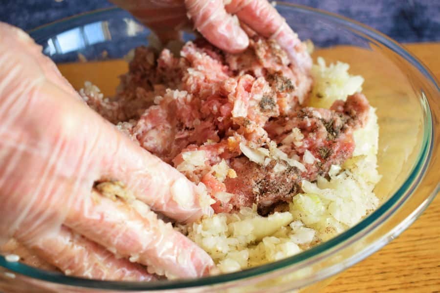 Cabbage roll ingredients getting mixed in clear glass bowl, wooden background.