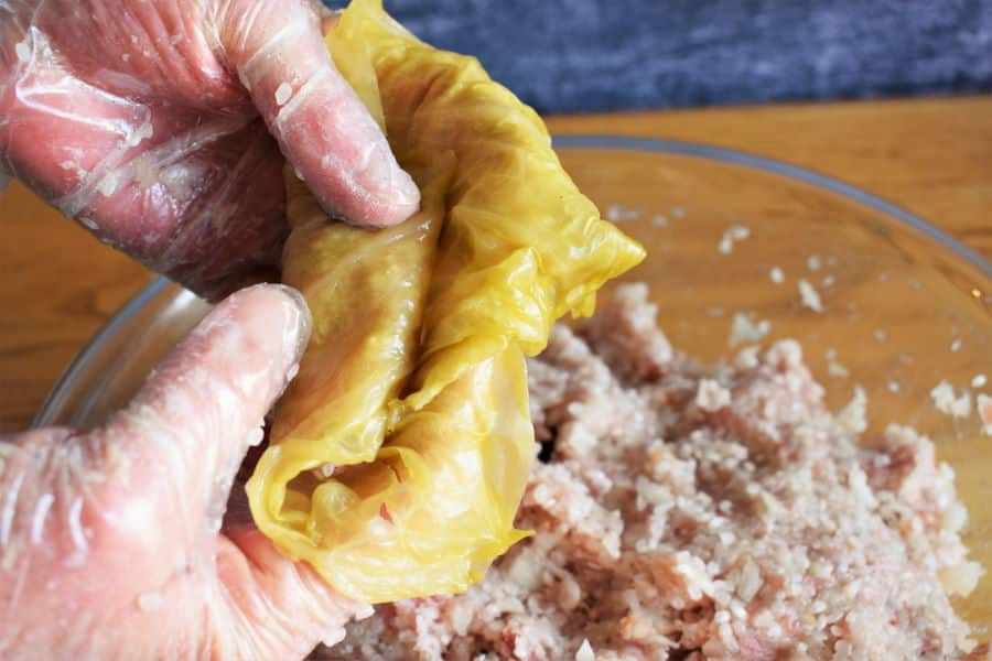 Cabbage roll being rolled up with gloved hands.