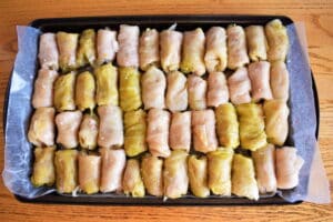 Cabbage rolls on a wax paper-lined baking sheet, on wooden table.