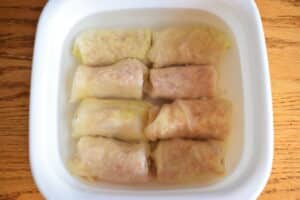 Cabbage rolls in a casserole dish with hot water, wooden background.