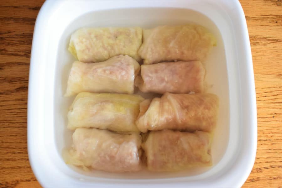 Cabbage rolls in a casserole dish with hot water, wooden background.