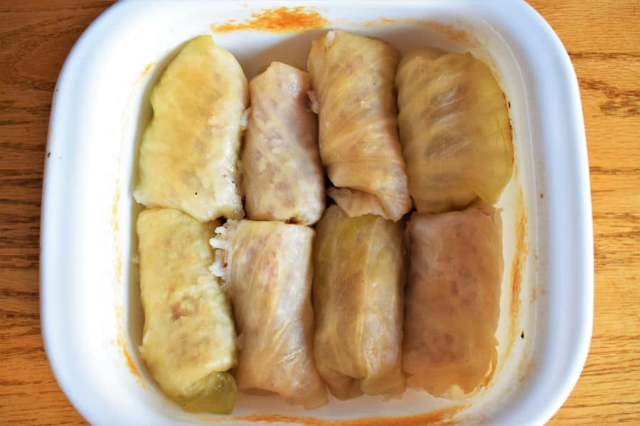 Baked cabbage rolls in a casserole dish, wooden background.